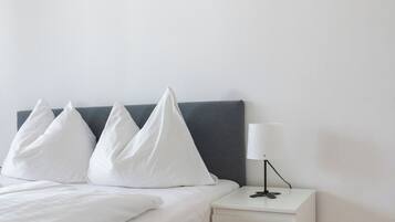 Een bed met witte lakens, een grijze hoofdbord en een nachtkastje met een lamp.