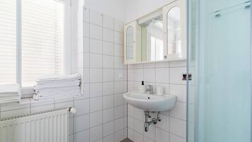 A bathroom with white tiles, a sink, a mirror, and a window with blinds.
