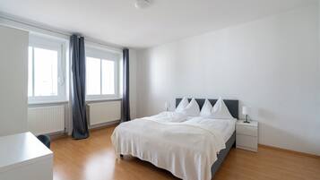 A modern bedroom with a bed, bedside lamps, a radiator, and a window with curtains.
