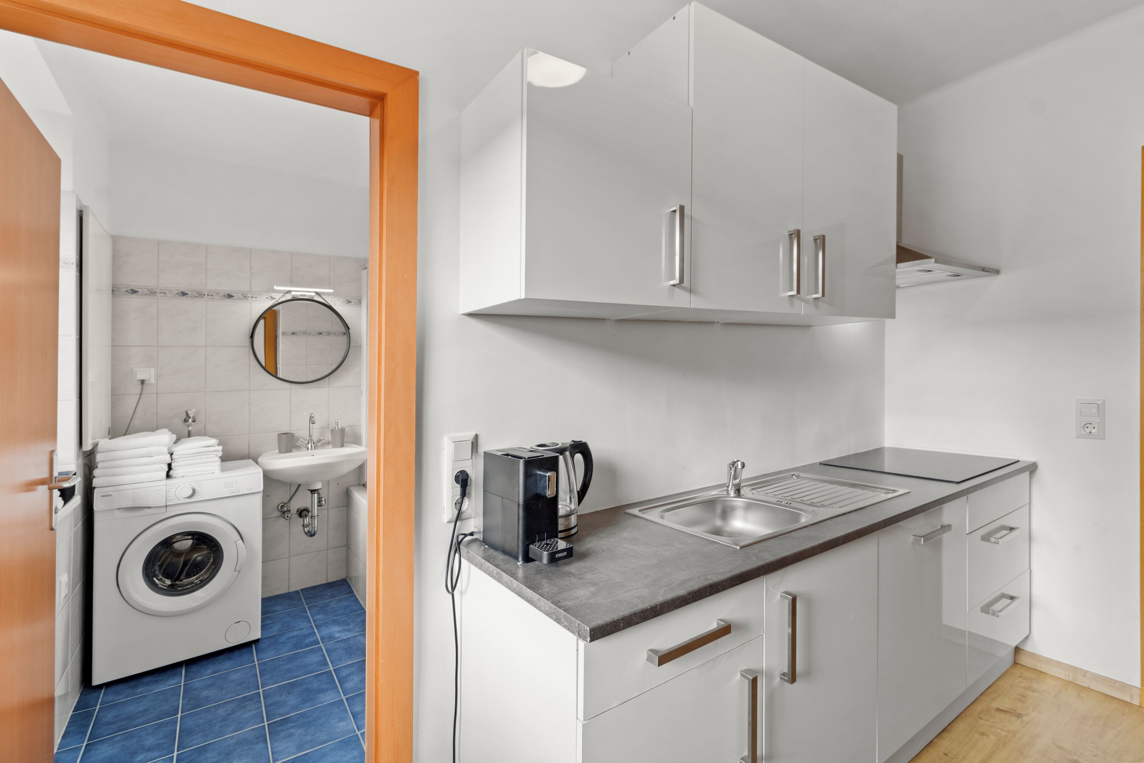 Cocina compacta con lavadora, cafetera y lavabo.
