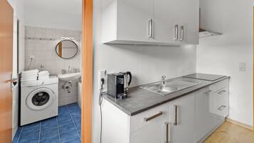 Cocina compacta con lavadora, cafetera y lavabo.