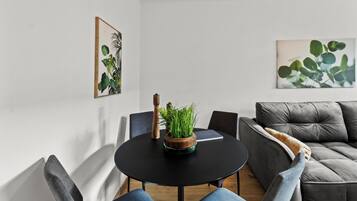 A modern living room with a round black table, a grey sofa, and two armchairs. There are two framed botanical prints on the walls.