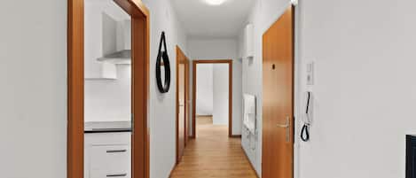 Un pasillo con suelo de madera, paredes blancas y una zona de cocina con armarios blancos y una estufa.