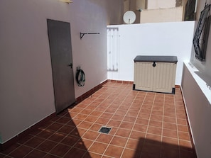 Un petit espace ext érieur clos, doté d’un sol carrelé, d’une porte, d’un tuyau fixé au mur et d’un petit espace de rangement.
