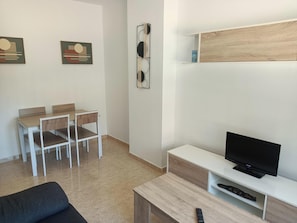 Un salon moderne avec un téléviseur, un canapé, une table à manger avec des chaises et des œuvres d’art accrochées aux murs.