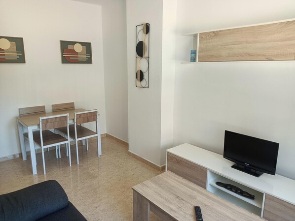 A modern living room with a TV, a sofa, a dining table with chairs, and artwork on the walls.