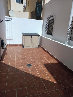 Een betegeld terras met een kleine opbergunit, een schotelantenne en een metalen poort.