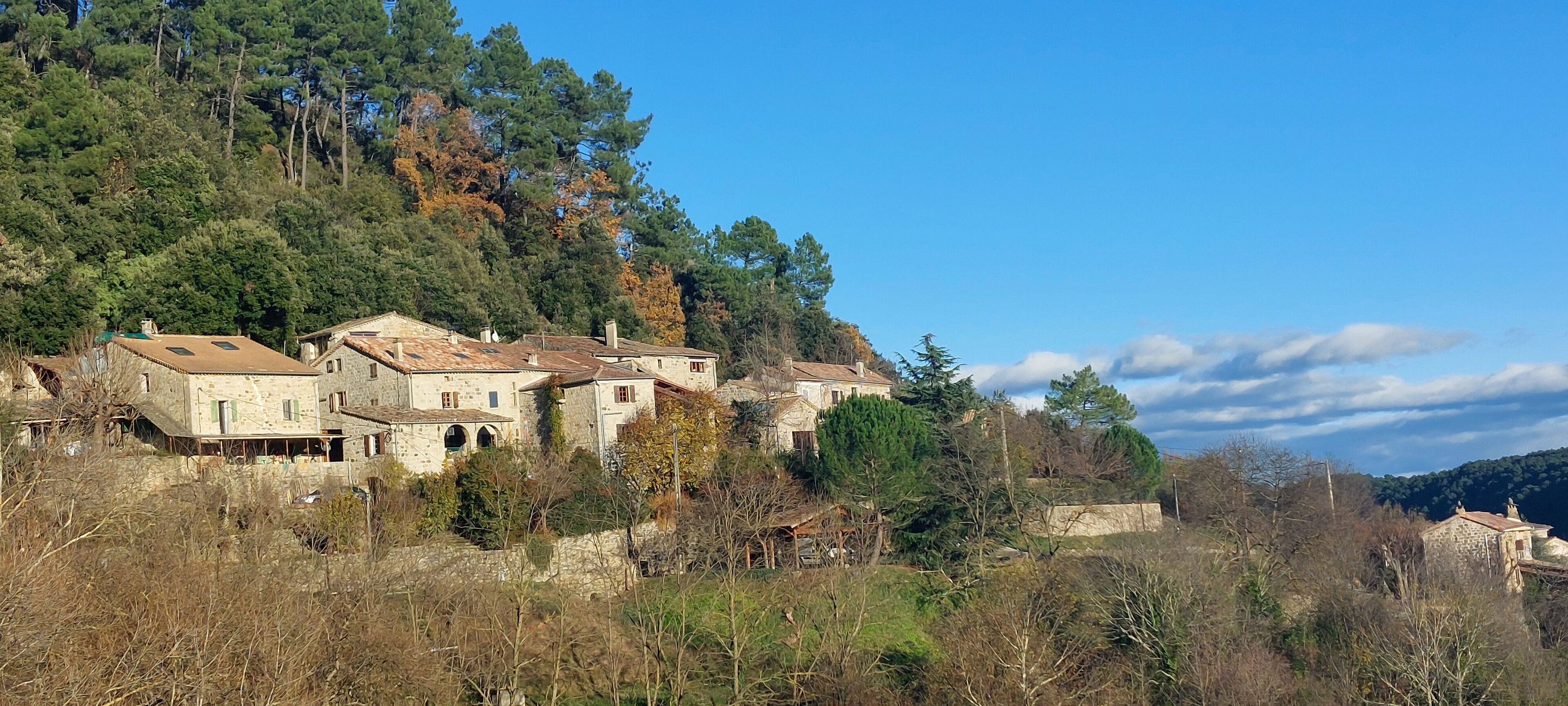 Um conjunto de edifícios de pedra com arquitetura tradicional, rodeado por árvores e colinas.