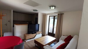 Ein kompakter Wohnraum mit Küchenzeile, Fernseher, Esstisch und einer Couch.