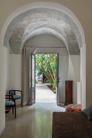 Corredor interno que leva a um quarto com uma cama, uma cadeira e um armário de madeira.