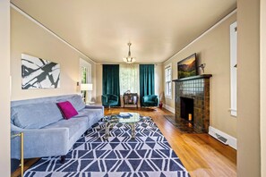 Ein Wohnzimmer mit einer Couch, einem gemusterten Teppich, einem Kamin und Blick ins Freie.