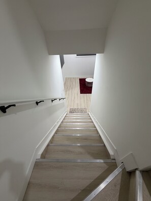 Eine enge Treppe mit Holzboden und Metallgeländern, die zu einem Raum mit einem gemusterten Teppich und einem kleinen Rundtisch führt.