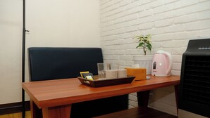 Ett träbord med ett bricka fullt av föremål, en rosa vattenkokare och en svart luftkonditioneringsapparat i ett rum med en vit tegelvägg.