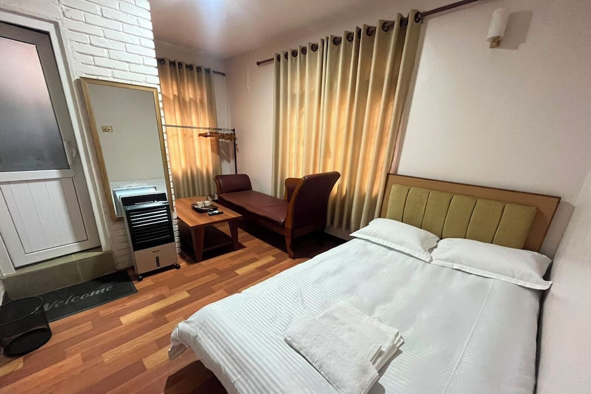 Une chambre dâhĂŽtel comprenant un lit, un bureau, une chaise, une armoire et une fenĂȘtre avec des rideaux.