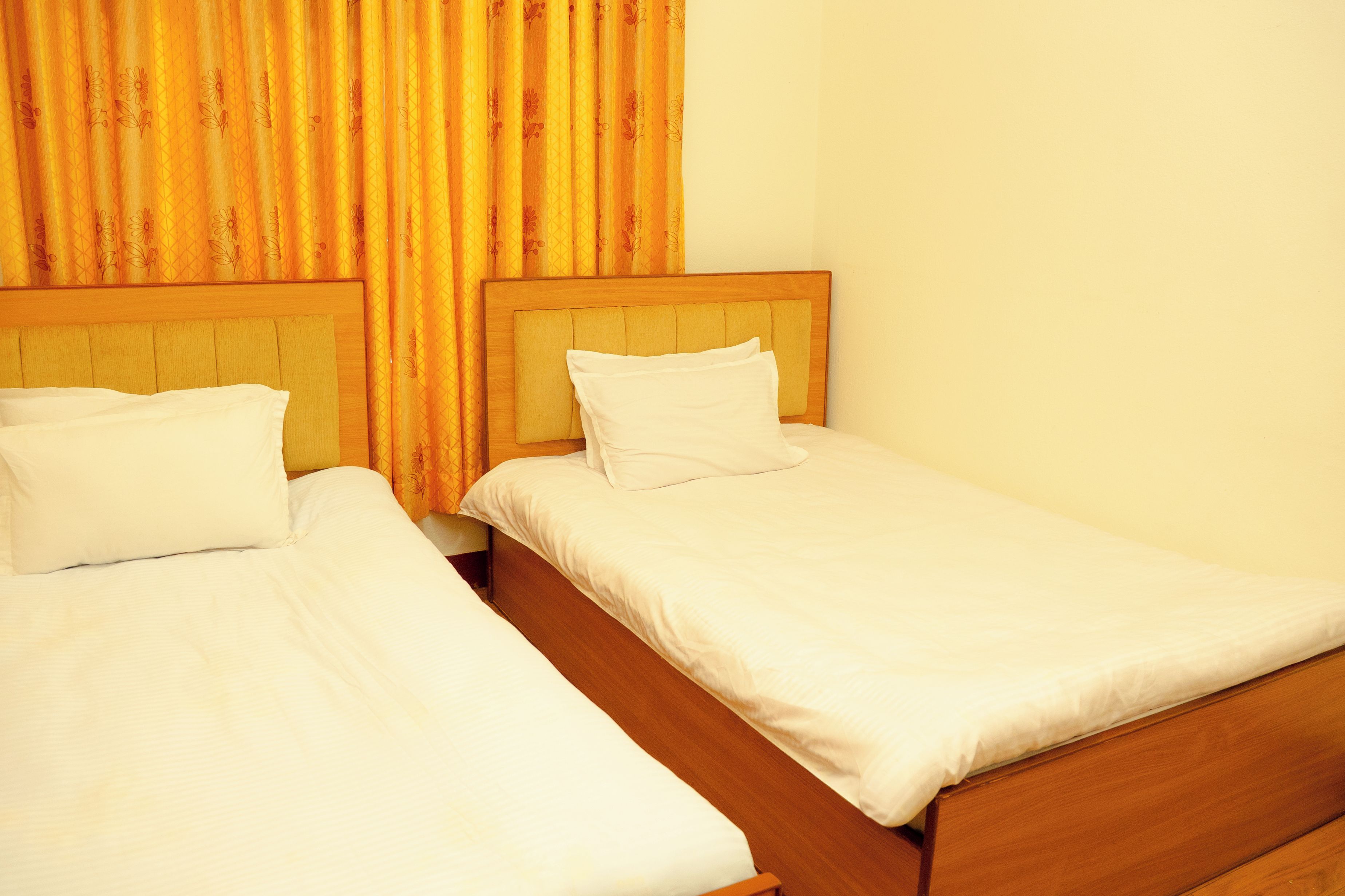 Two single beds with wooden headboards in a room with yellow curtains.