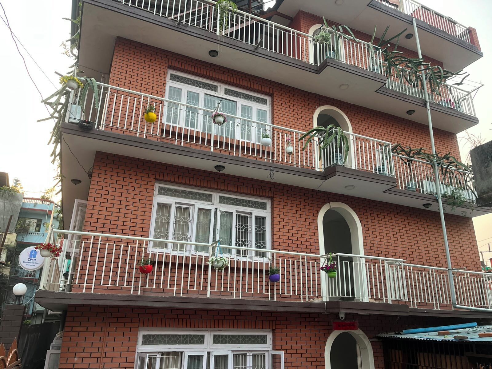 Un edificio de varios pisos con balcones, ventanas y algunas plantas en macetas.