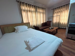 Hotellihuone, jossa on sänky, tuoli, pöytä ja lämmitin.