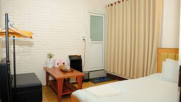 A hotel room with a bed, a desk with a kettle and a tray, a suitcase, a heater, and a coat rack.