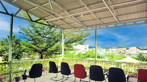A covered outdoor seating area with chairs, a view of buildings, and greenery. - Cozy Twin Escape With Free Wifi and Parking (Bukittinggi)