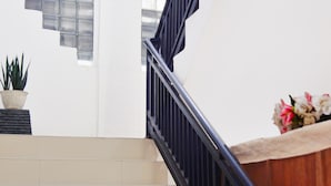 A staircase with a black railing, a potted plant, and a vase with flowers at the landing. - Cozy Twin Escape With Free Wifi and Parking (Bukittinggi)