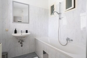 Un baño con lavamanos blanco, espejo y bañera con ducha.