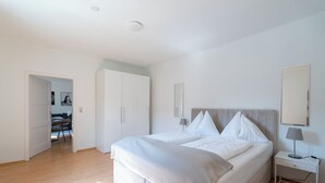 Une chambre à coucher comprenant un lit, des tables de chevet, une armoire et une porte donnant sur un coin repas.