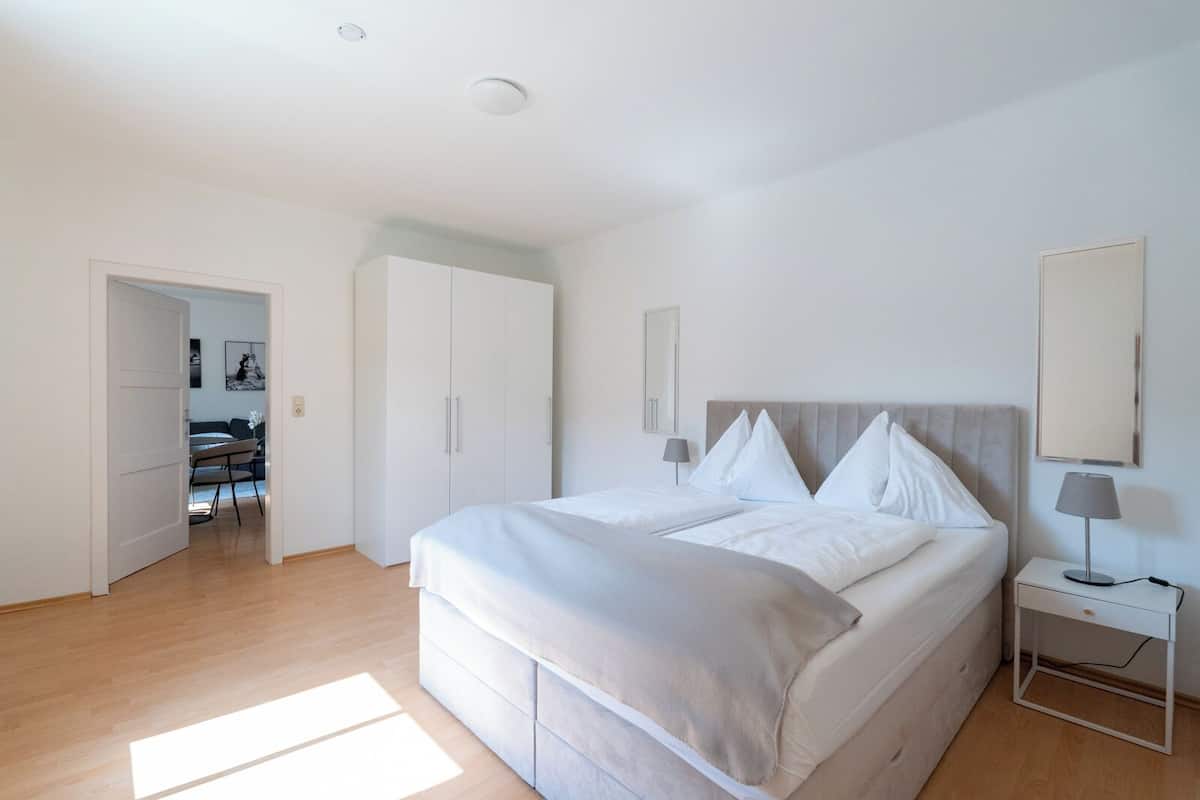 Un dormitorio con cama, mesitas de noche, un armario y una puerta que da a un comedor.
