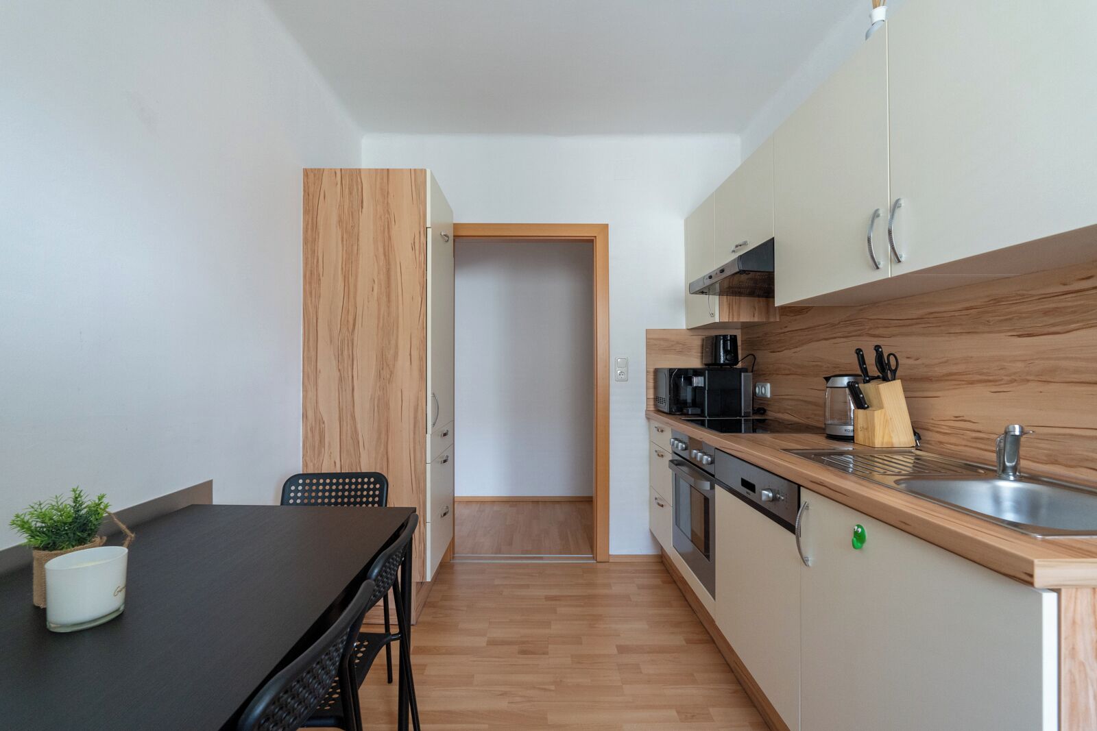 A compact kitchen with a dining area, wooden cabinets, a microwave, a coffee maker, and a sink.