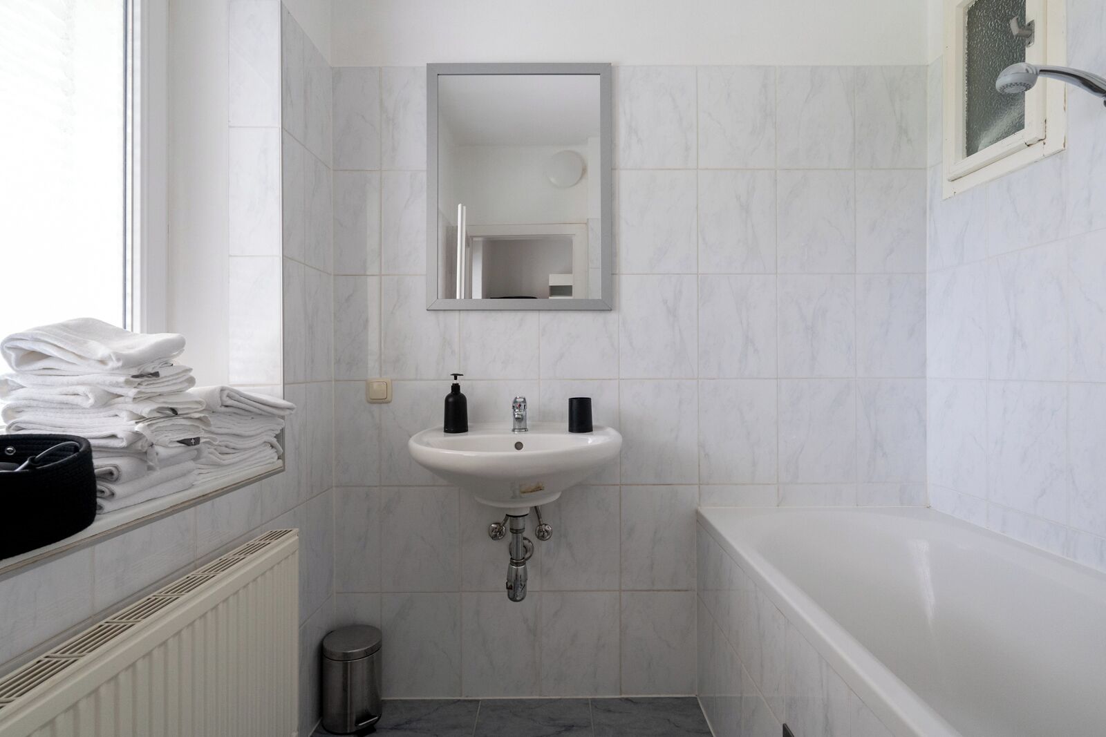 Een badkamer met een witte wastafel, een spiegel, een stapel handdoeken en een douche.