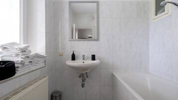 Een badkamer met een witte wastafel, een spiegel, een stapel handdoeken en een douche.