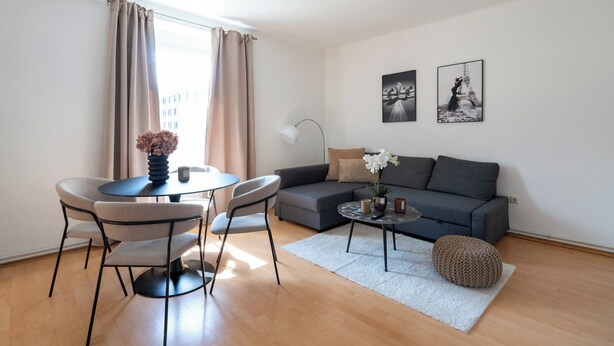 Un salon moderne avec un canapé gris, une table basse ronde et un coin repas avec des chaises.