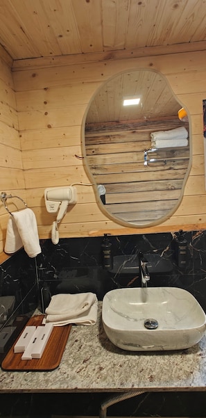 Une salle de bain avec un plafond en bois, un miroir rond, un lavabo avec un plan de toilette en marbre et un porte-serviettes.