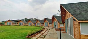 A row of wooden cabins with a paved walkway, each with a window and a door. - Karibu Resort Karjat (Karjat)