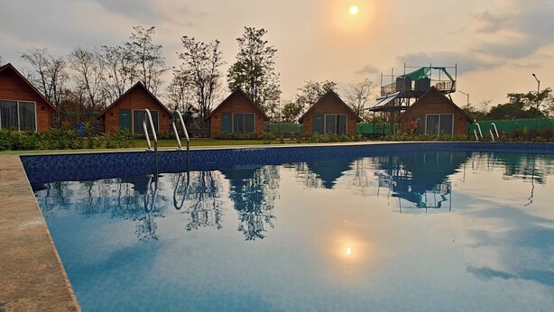 A swimming pool with wooden cabins in the background. - Karibu Resort Karjat (Karjat)