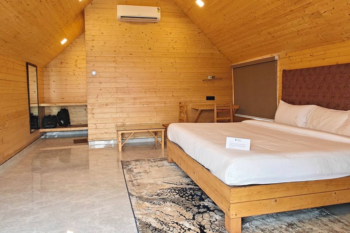 Puinen mökkimäinen makuuhuone, jossa on sänky, pieni pöytä ja tuoli.