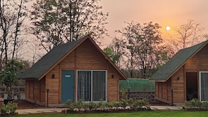 Two wooden cabins with large windows, a stone wall, and a solar panel array. - Karibu Resort Karjat (Karjat)