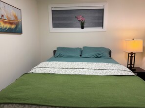 Ein ordentlich bezogenes Bett mit einer grün-weißen Decke, einem türkisfarbenen Kopfkissen und einem kleinen Topfpflanzchen auf dem Nachttisch.