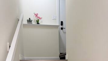 Un escalier avec des marches en bois et une rampe blanche, menant à un palier où se trouve une petite plante en pot et un interrupteur.