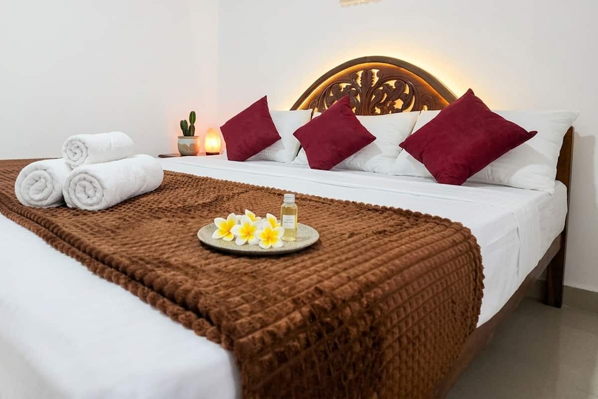 A neatly made bed with white linens, a brown blanket, and a tray with flowers and a bottle.