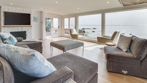 Ein geräumiges Wohnzimmer mit großem Fenster zum Strandblick, einem Kamin und einer gemütlichen Sitzecke.