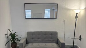 Un sofá gris, una planta en maceta, una lámpara de pie y un cuadro en la pared.