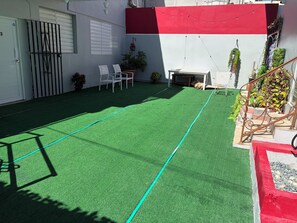 A courtyard with artificial turf, white chairs, a small table, and a staircase with red accents. - Central & Modern Apt in Miramar (San Juan)