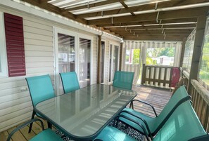 Eine überdachte Terrasse mit Glastisch und Stühlen, einer Holzterrasse und Blick auf den Garten.