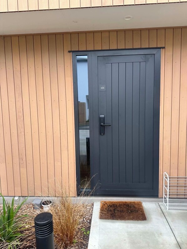 A modern building with a dark grey door, a small entryway with a doormat, and a metal railing to the right.