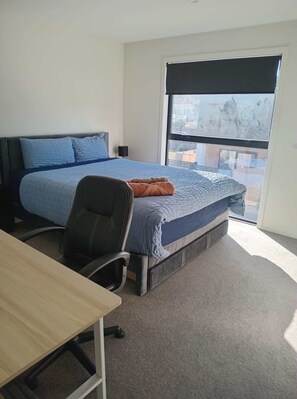 A bedroom with a bed, a desk, a chair, and a large window.