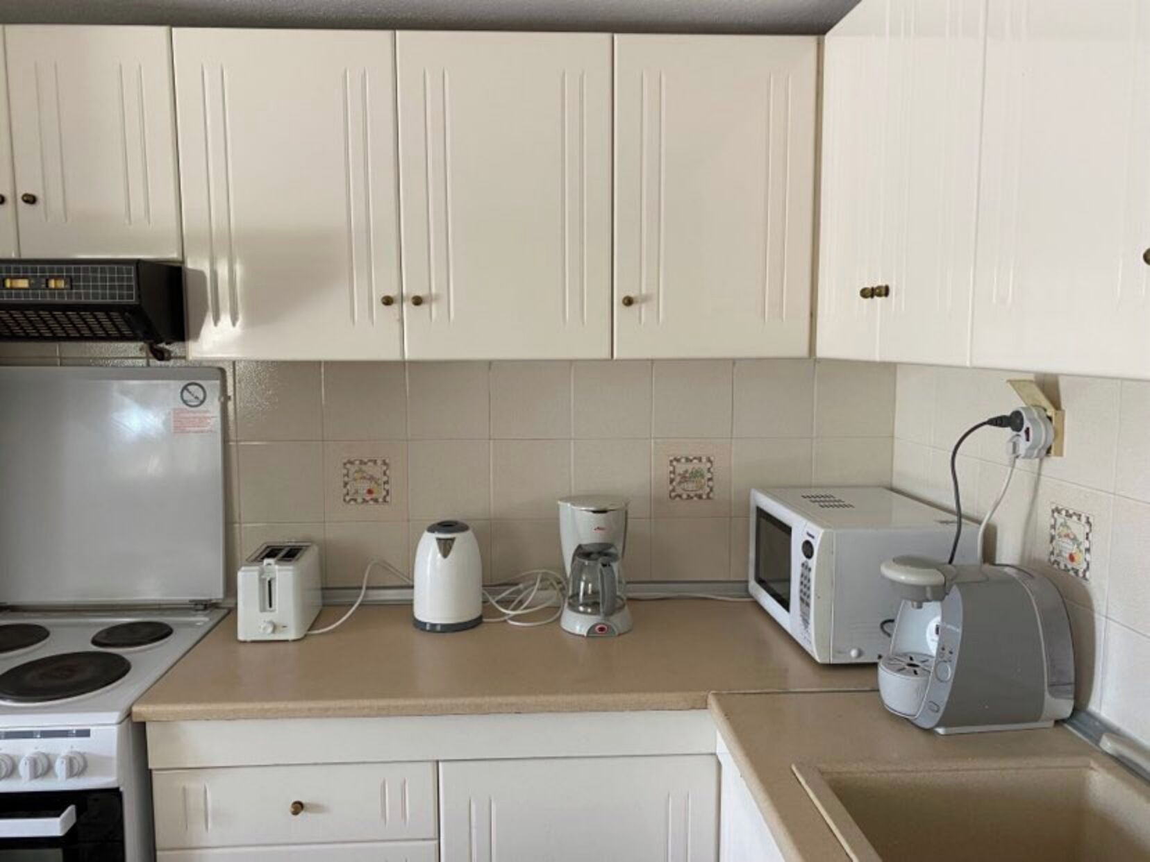 A kitchen with white cabinets, a stove, a microwave, a toaster, and a coffee maker.