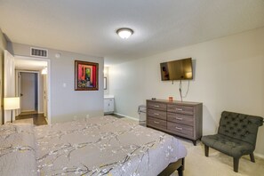 Un dormitorio con cama, cómoda, silla, televisor y una obra de arte en la pared.