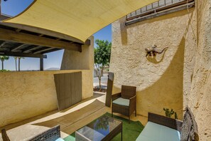 An outdoor patio area with wicker furniture, a glass-top table, and a textured wall.