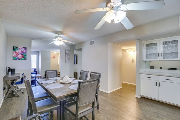 A dining area with a wooden table, chairs, ceiling fans, and a kitchen with white cabinets.