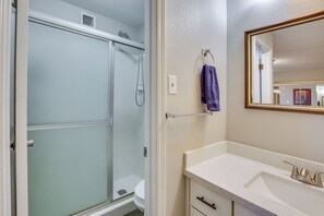 A bathroom with a glass shower enclosure, a white sink with a gold faucet, and a mirror with a gold frame.